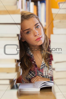 Unsmiling pretty student studying between piles of books