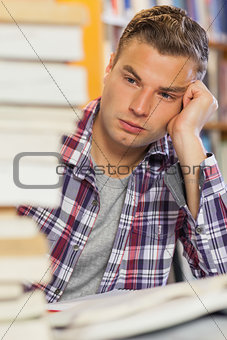 Tired handsome student studying between piles of books