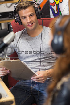 Attractive happy radio host interviewing a guest holding clipboard