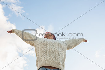 Woman in white sweater stretching her arms against sky