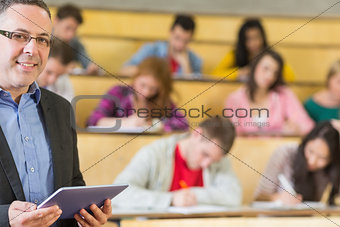 Teacher using tablet PC with students sitting at lecture hall