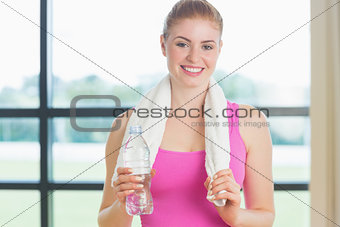 Portrait of a woman with towel around neck holding water bottle in fitness studio