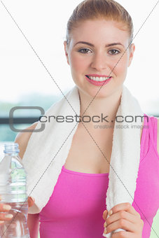 Woman with towel around neck holding water bottle in fitness studio