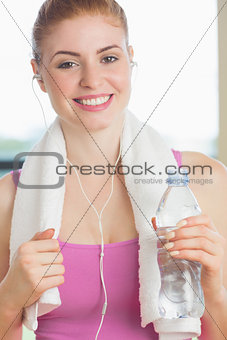 Woman with towel around neck holding water bottle in fitness studio