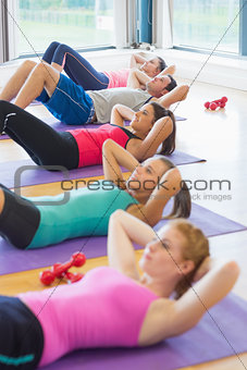Sporty fitness class doing sit ups on exercise mats