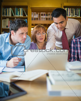 Mature students with teacher and laptop in library