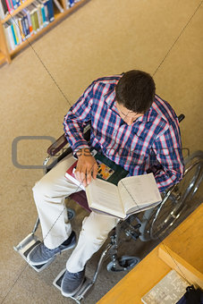 Man in wheelchair reading a book in library