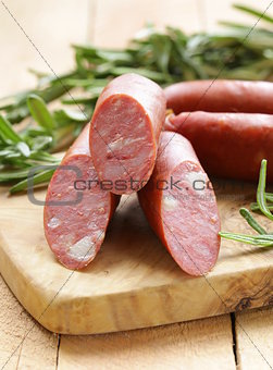 Dried sausage with  fresh rosemary on a wooden background