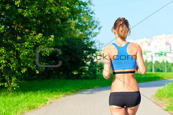 athletic girl in a top and shorts running on the road in the park, not far from the city