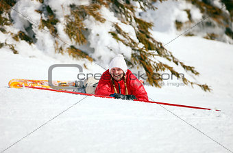 Cute young female skier looking at the camera after falling down on mountain slope