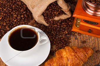 Coffee cup with a croissant and fresh coffee beans
