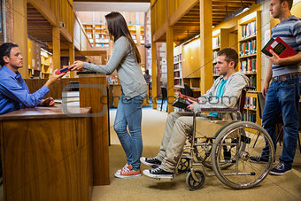 Students with handicapped man in row at library counter