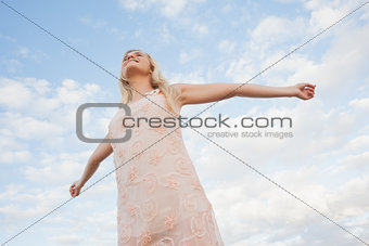 Young woman in summer dress stretching arms against sky