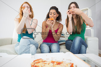 Happy young female friends eating pizza at home