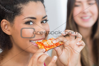 Close up portrait of a female eating pizza with blurred friend