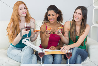 Happy young female friends with pizza and wine at home