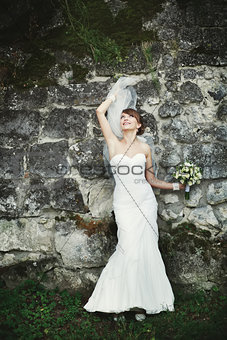 Young bride playing with veil against rock wall.
