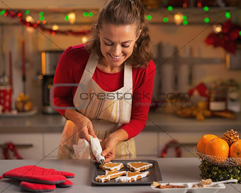 Happy young housewife decorating christmas cookies in kitchen