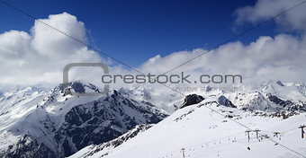 Panoramic view on ski slope and cloudy mountains at nice sun day