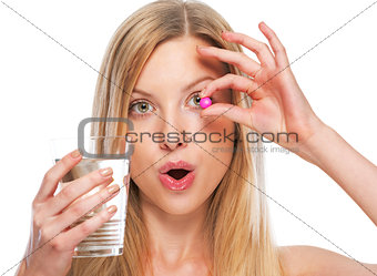 Portrait of teenage girl with cup of water showing pill