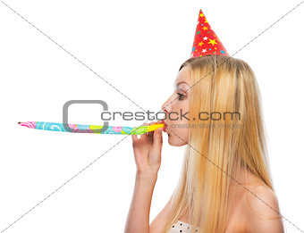 Profile portrait of teenage girl in cap blowing in party horn bl