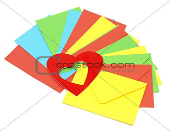 A red heart on pile colorful envelopes over white background