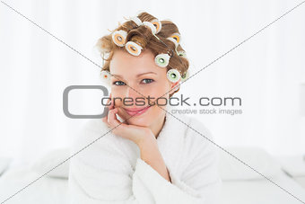 Woman in bathrobe and hair curlers sitting on bed