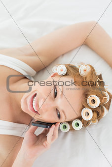 Relaxed woman in hair curlers using cellphone in bed