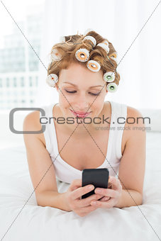 Relaxed woman in hair curlers text messaging in bed