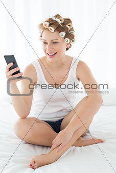 Relaxed woman in hair curlers text messaging on bed