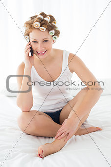 Beautiful woman in hair curlers using cellphone on bed