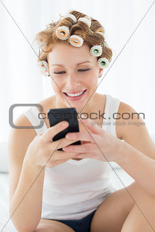 Woman in hair curlers text messaging on bed