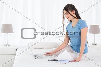 Woman paying her bills online with laptop in bedroom