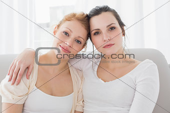 Smiling female friends with arm around in living room