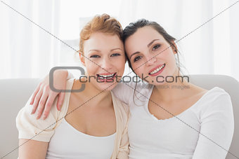 Happy female friends with arm around in the living room