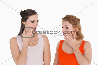 Two young shocked female friends with hand over mouth