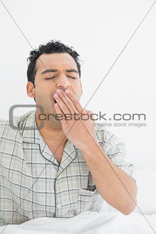 Young man yawning in bed