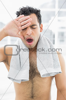 Shirtless man yawning with eyes closed in bedroom
