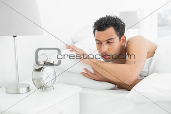 Sleepy man looking at the alarm clock in bed