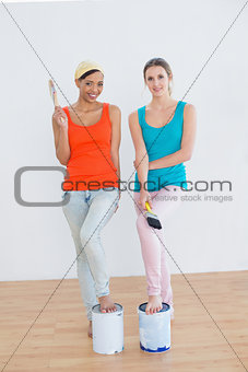 Female friends with paint brushes and cans in a new house