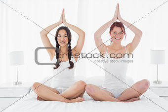 Two women sitting with joined hands over head on bed