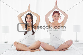 Two women sitting with joined hands over head on bed