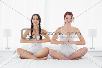 Two young women sitting with joined hands on bed