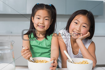 Portrait of two smiling girls sitting with bowls in kitchen
