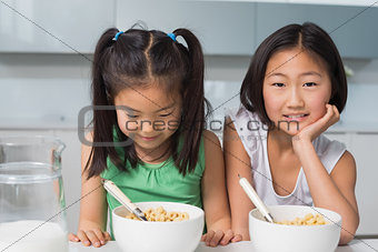 Two smiling young girls sitting with bowls in kitchen