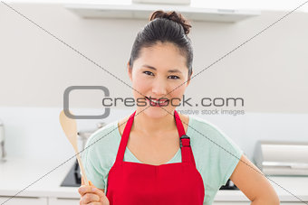 Smiling woman in red apron with a wooden spoon in kitchen