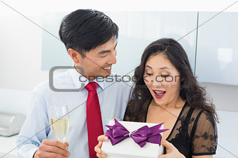 Shocked woman opening a gift box by man with champagne