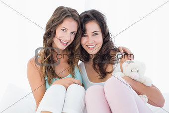Female friends sitting on bed with arm around