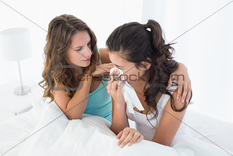 Woman consoling a crying female friend in bed