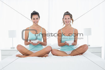 Female friends with bowls sitting on bed
